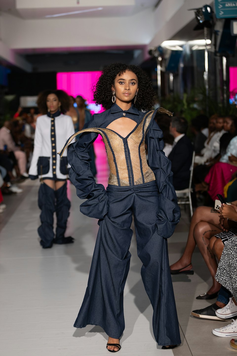 Model wearing an avant-garde denim outfit walks a fashion runway.