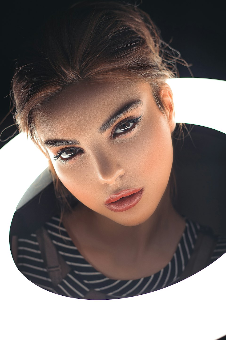 Woman with dark hair and defined makeup wearing a striped top.