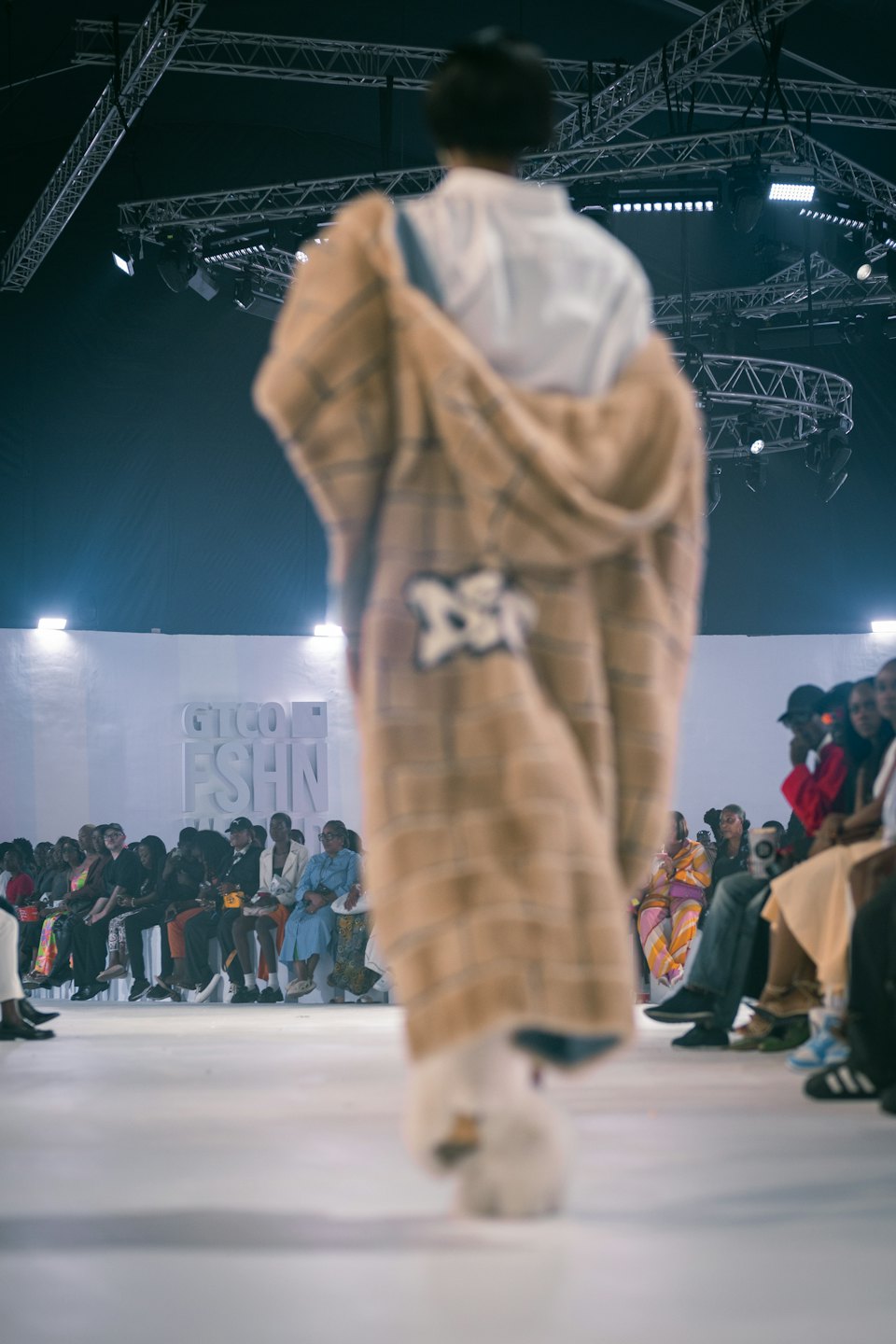 Model in a checkered coat walks down a fashion runway.